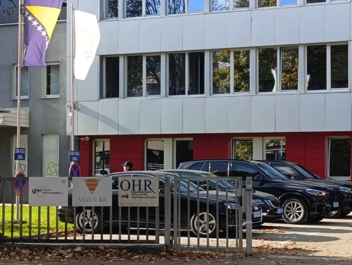 Zgrada Ureda Visokog predstavnika (OHR) u Bosni i Hercegovini sa zastavama Bosne i Hercegovine i Kosova, te parkiranim crnim automobilima ispred.