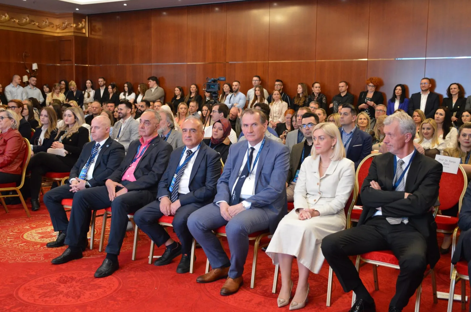 Publika sjedi u sali tokom konferencije, slušaju predavača.
