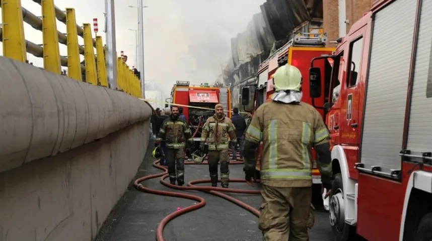 Vatrogasci u zaštitnoj opremi raspoređeni oko vatrogasnih vozila i crijeva na mjestu požara.