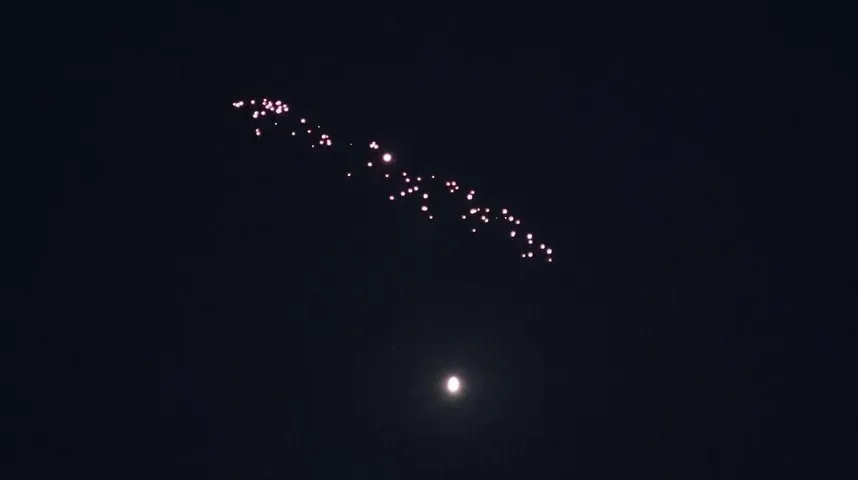 Iz daljine se vide svjetlosni tragovi vatrometa koji se šire po tamnom nebu, blizu njih je i puni Mjesec