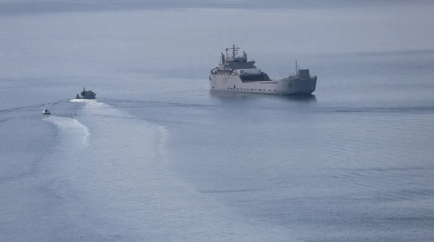 Veliki vojni ili teretni brod plovi mirnim morskim prostranstvom, praćen s dva manja čamca.