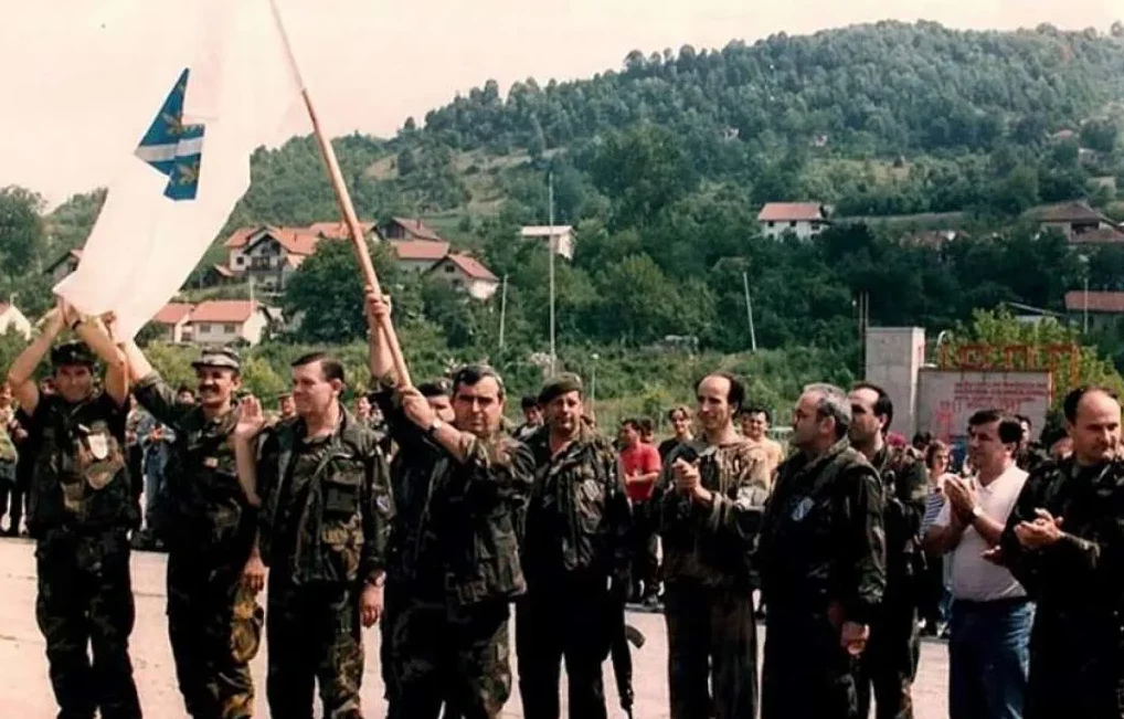 Grupa vojnika drži zastavu sa plavo-bijelim motivima.