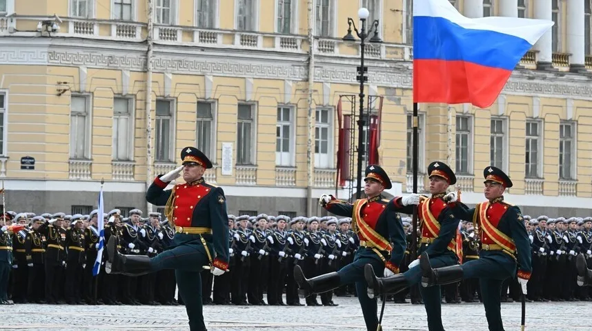 Vojnici u svečanim uniformama marširaju ispred zgrade sa ruskom zastavom u pozadini.