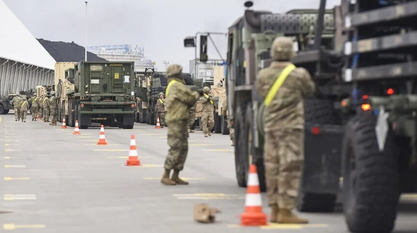 Vojnici u vojnim uniformama stoje pored niza vojnih vozila, uključujući kamione i prikolice.