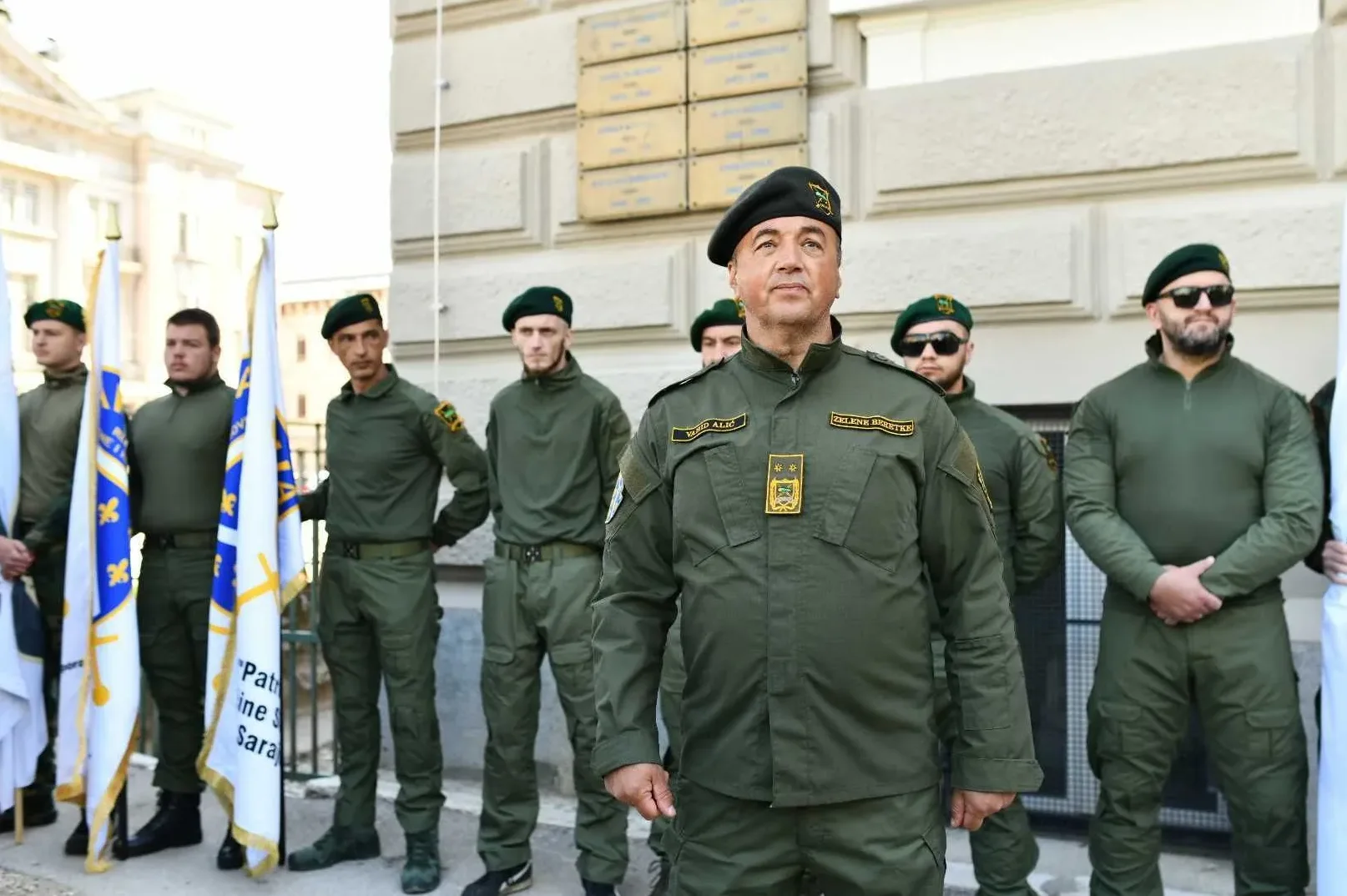 Vojnici Oružanih snaga Bosne i Hercegovine u zelenim uniformama i beretkama, stoje pored zastava.