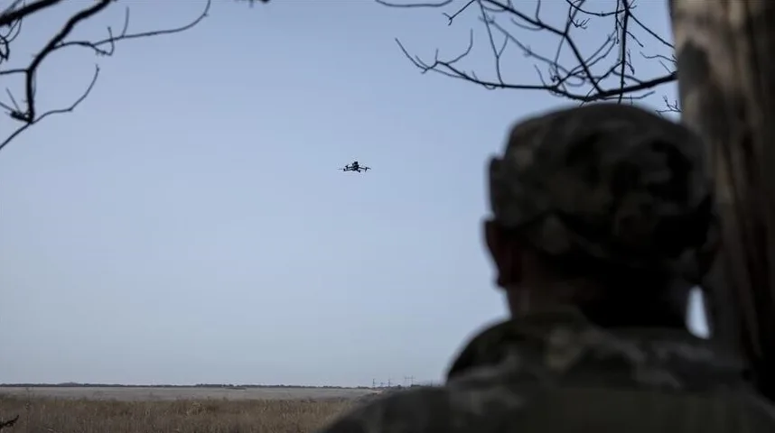 Vojnik u uniformi gleda u nebo gdje lebdi mali dron.