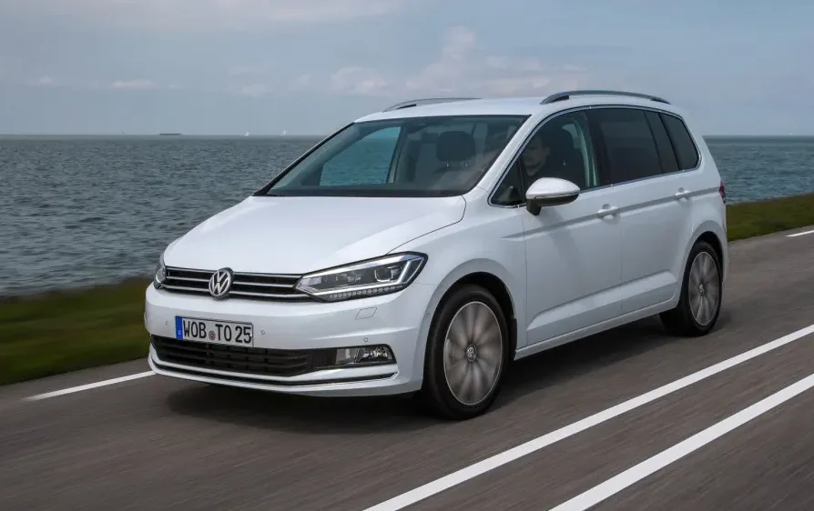 Bijeli Volkswagen Touran u pokretu na putu pored mora.