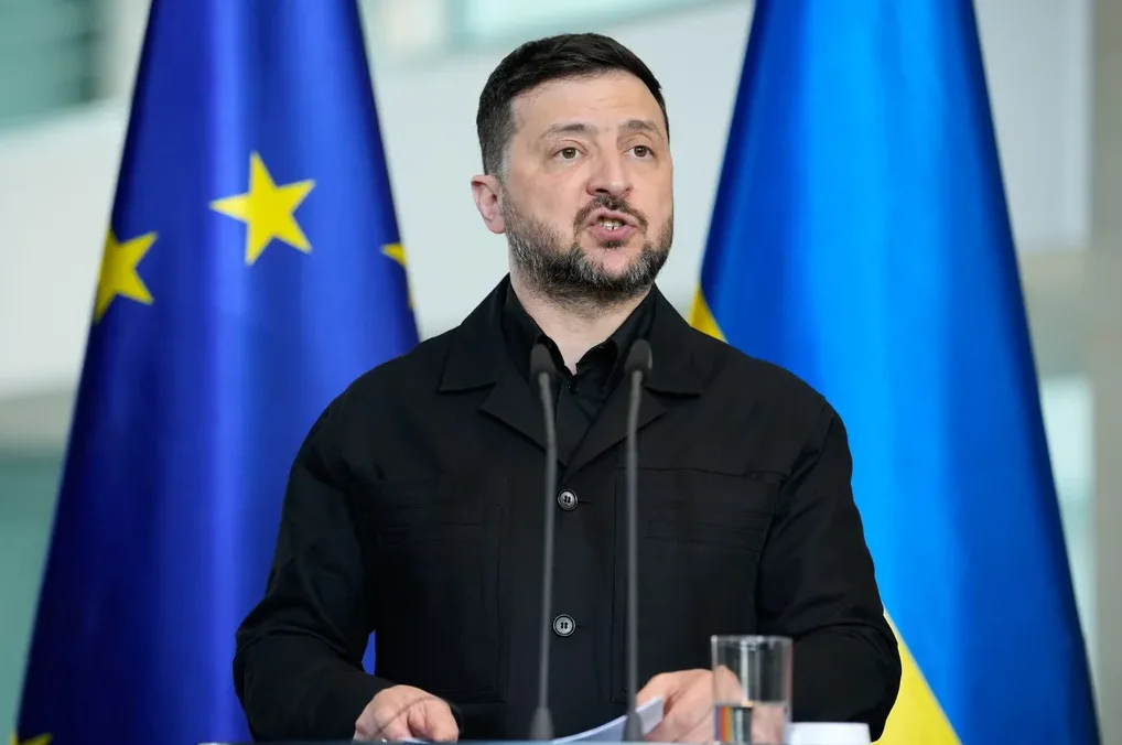 Volodimir Zelenski, predsjednik Ukrajine, govori iza podijuma sa miklofonima, dok su iza njega istaknute zastava Evropske unije i zastava Ukrajine.