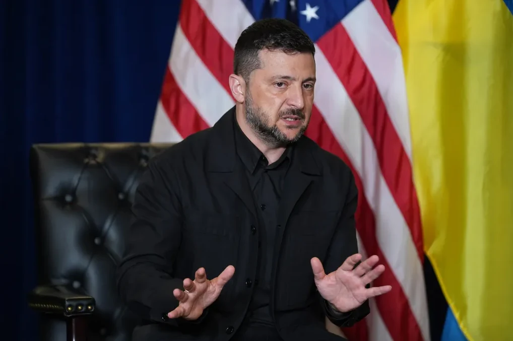 Volodimir Zelenski sjedi ispred zastava Sjedinjenih Američkih Država i Ukrajine.