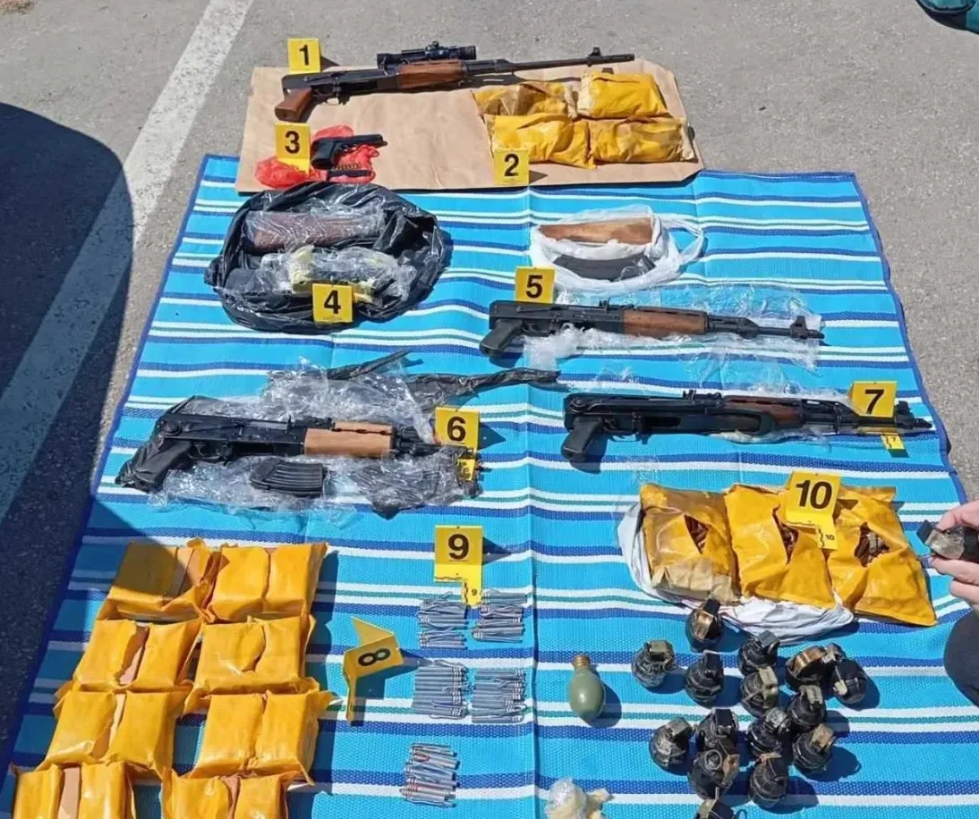 Zaplijenjeno oružje, uključujući automatske puške, pištolj, ručne bombe i municiju, izloženo na plavoj prostirci.