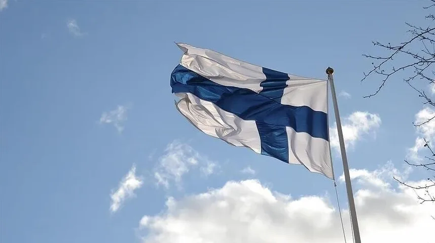 Finska zastava s plavim krstom na bijelom polju vijori se na jarbolu ispred neba s oblacima.