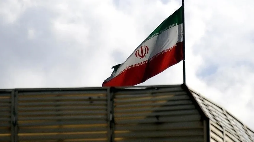 Zastava Islamske Republike Iran vijori se na jarbolu, sa zelenom, bijelom i crvenom horizontalnom prugom i nacionalnim grbom u sredini, na pozadini oblačnog neba.
