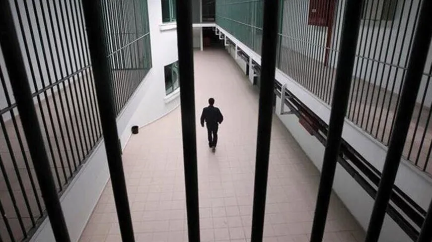 Čovjek u tamnom odijelu hoda unutar zatvorske ćelije kroz hodnik sa rešetkama.