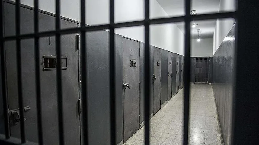 Pogled kroz zatvorske resetke na dugi hodnik sa nizom zatvorskih celija.