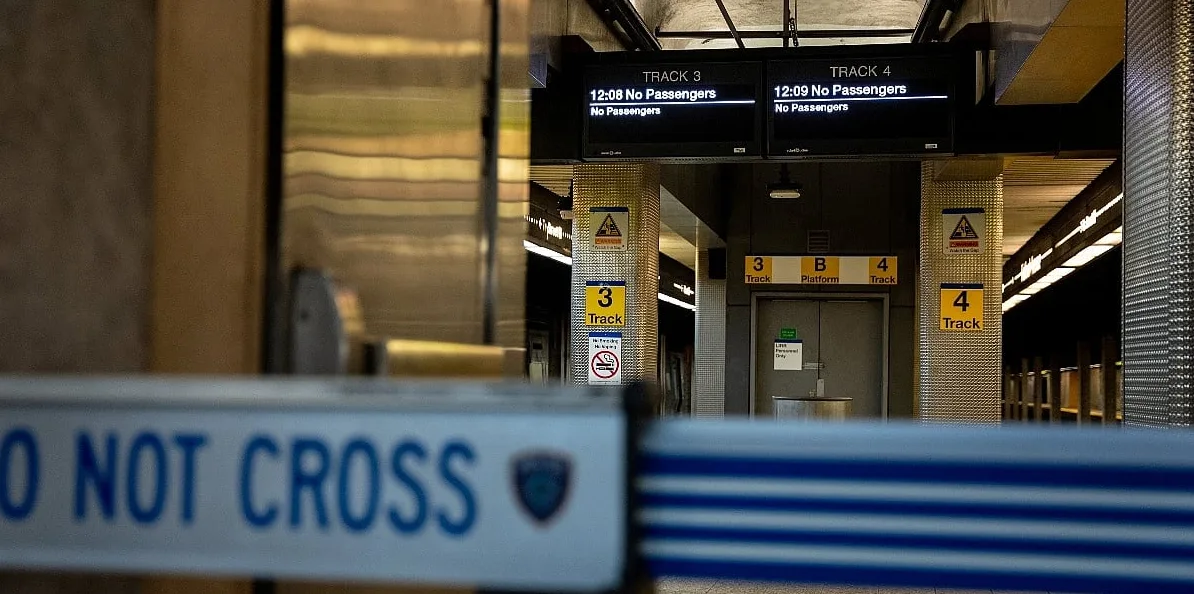 Trak s natpisom "DO NOT CROSS" ispred perona željezničke stanice s prikazanim informacijama o vozovima