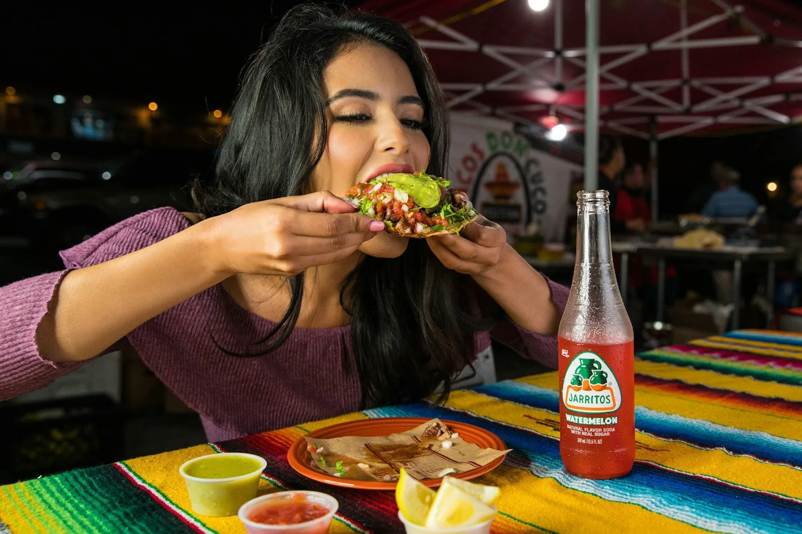 Mlada žena uživa u ukusnom tacu s avokadom i osvježavajućim pićem Jarritos od lubenice.