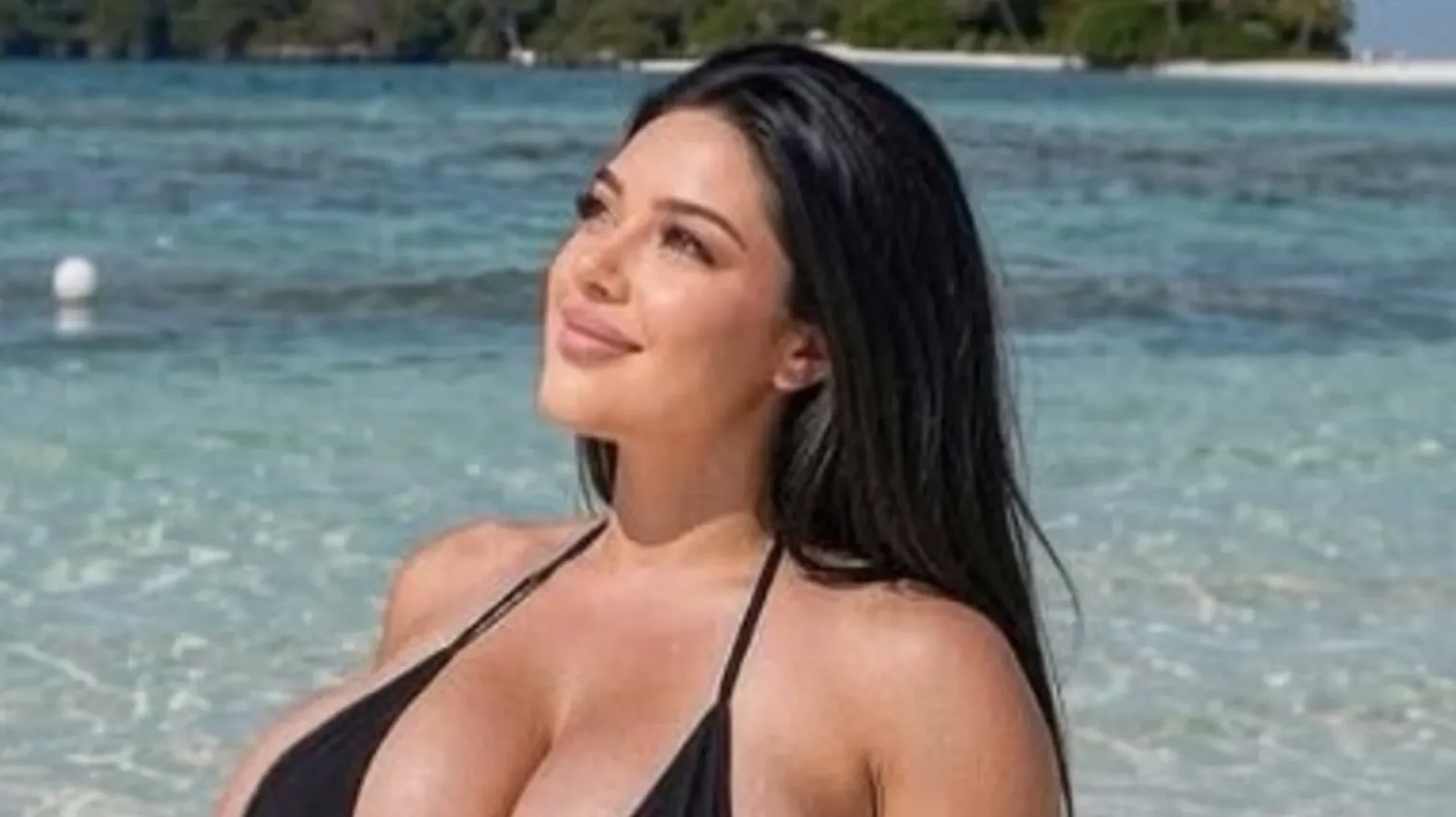 Mlada žena u crnom kupaćem kostimu na pješčanoj plaži, gleda prema gore prema suncu.