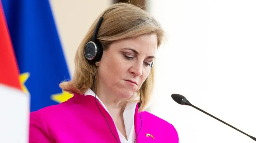 Žena u ružičastom sakou nosi slušalice i gleda prema dolje prema mikrofonu.