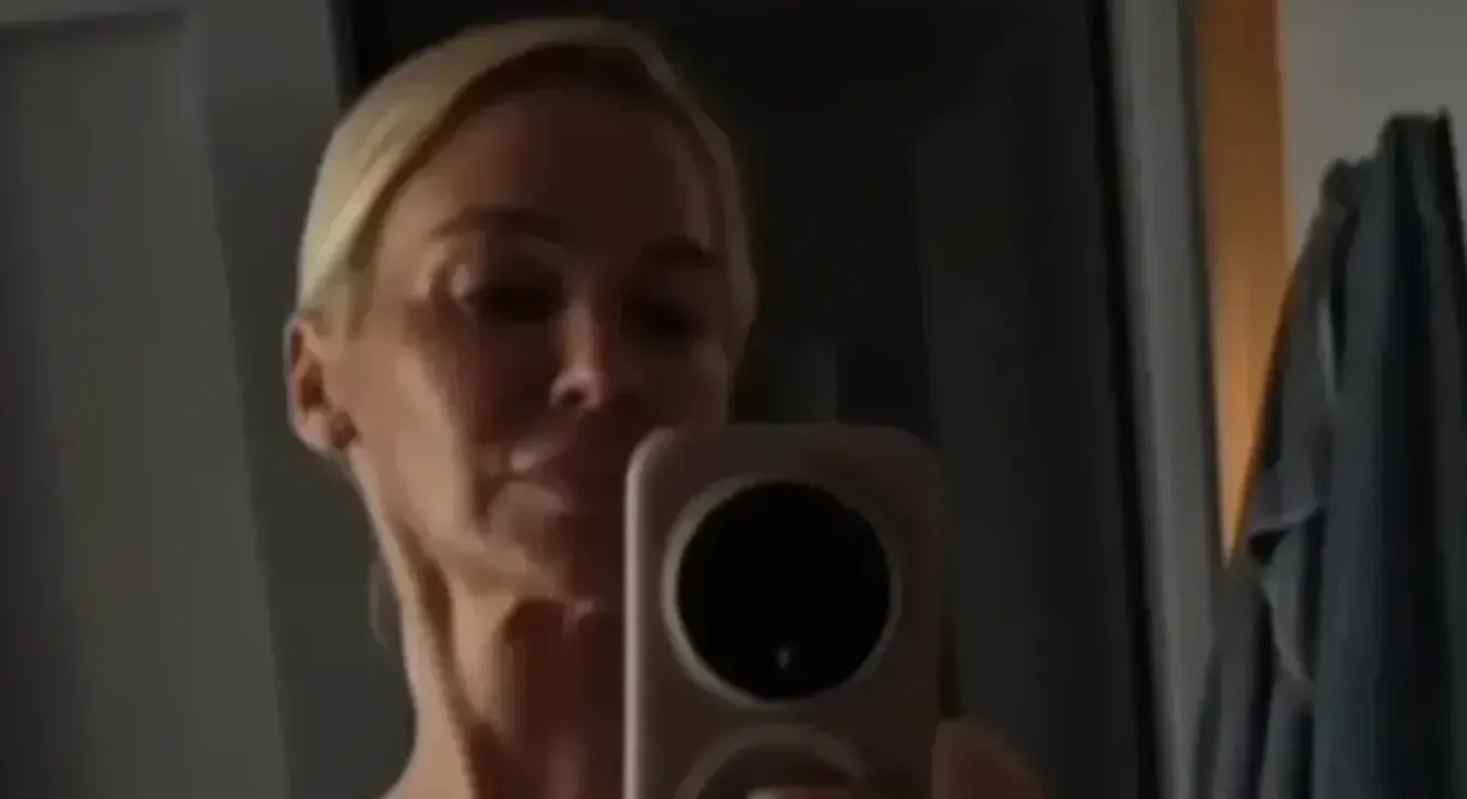 Žena sa plavom kosom i pametnim telefonom u ruci slika sebe u ogledalu.
