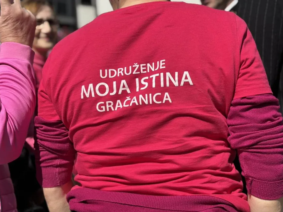 Žena nosi roze majicu kratkih rukava sa natpisom "UDRUŽENJE MOJA ISTINA GRAČANICA" bijelim slovima.