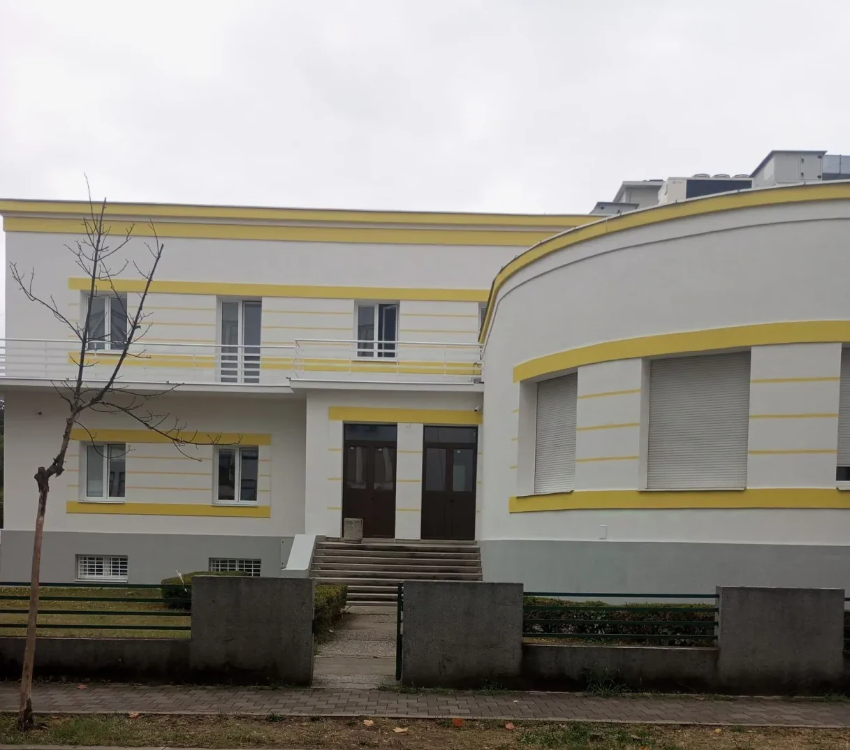 Moderna zgrada bijele boje sa upečatljivim zlatnim horizontalnim trakama i zakrivljenim dijelom fasade.