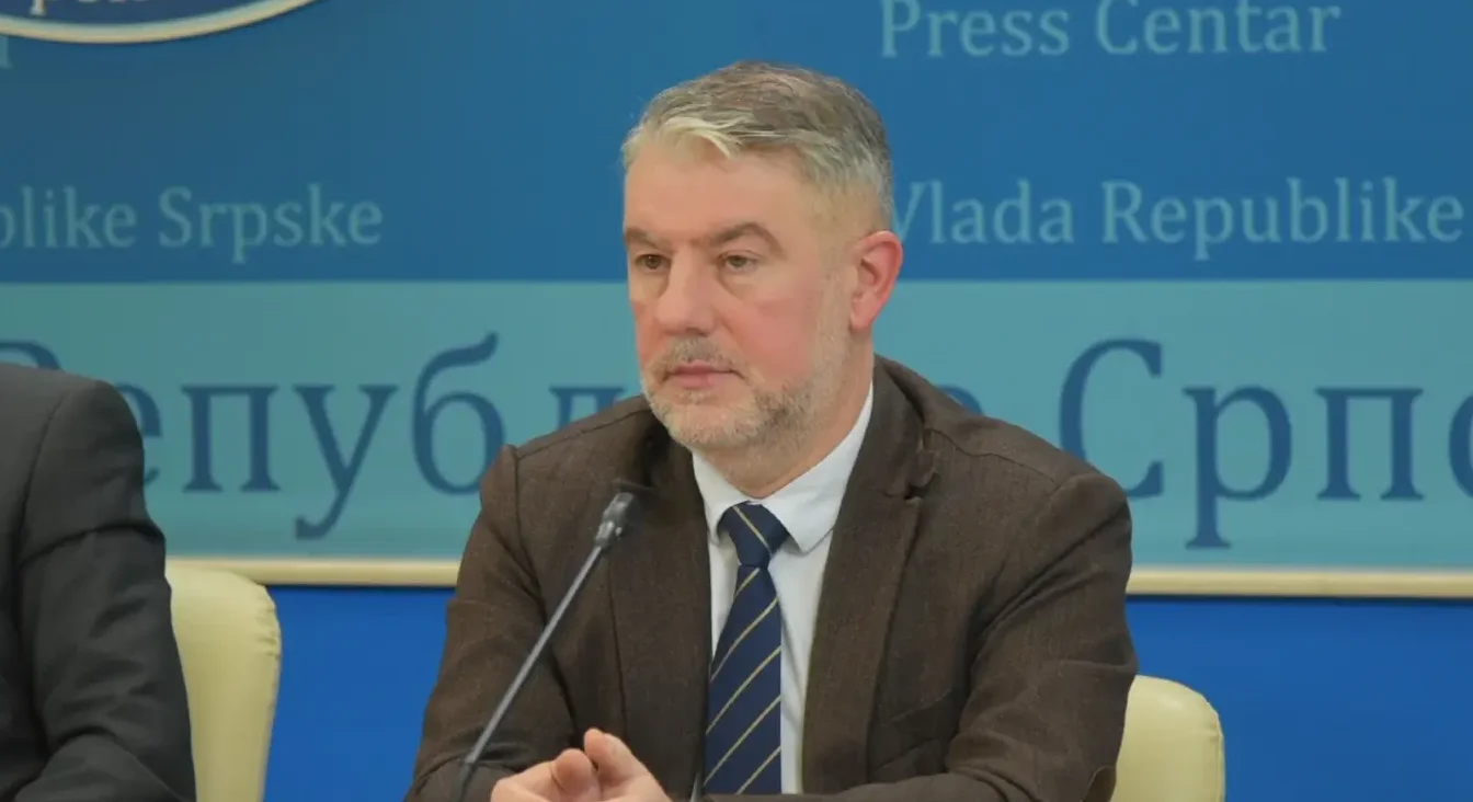 Muškarac srednje životne dobi sa sijedom kosom i bradom, obučen u smeđe odijelo i plavu kravatu sa prugicama, sjedi za govornicom ispred plave pozadine sa natpisom "Press Centar Vlade Republike Srpske".