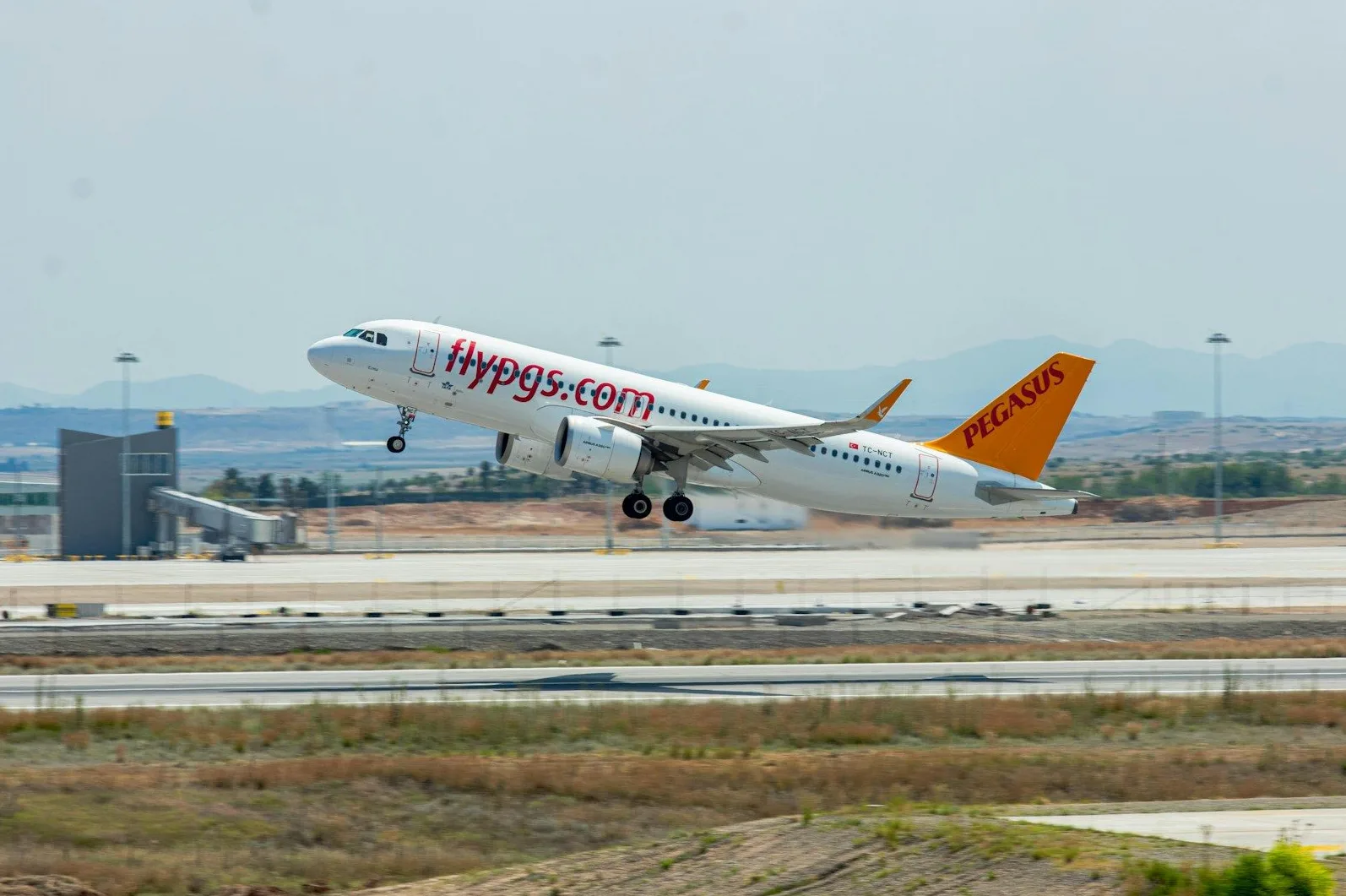 Bijeli avion Turkish Airlines Pegasusa sa narandžastim repom uzlijeće sa aerodroma.