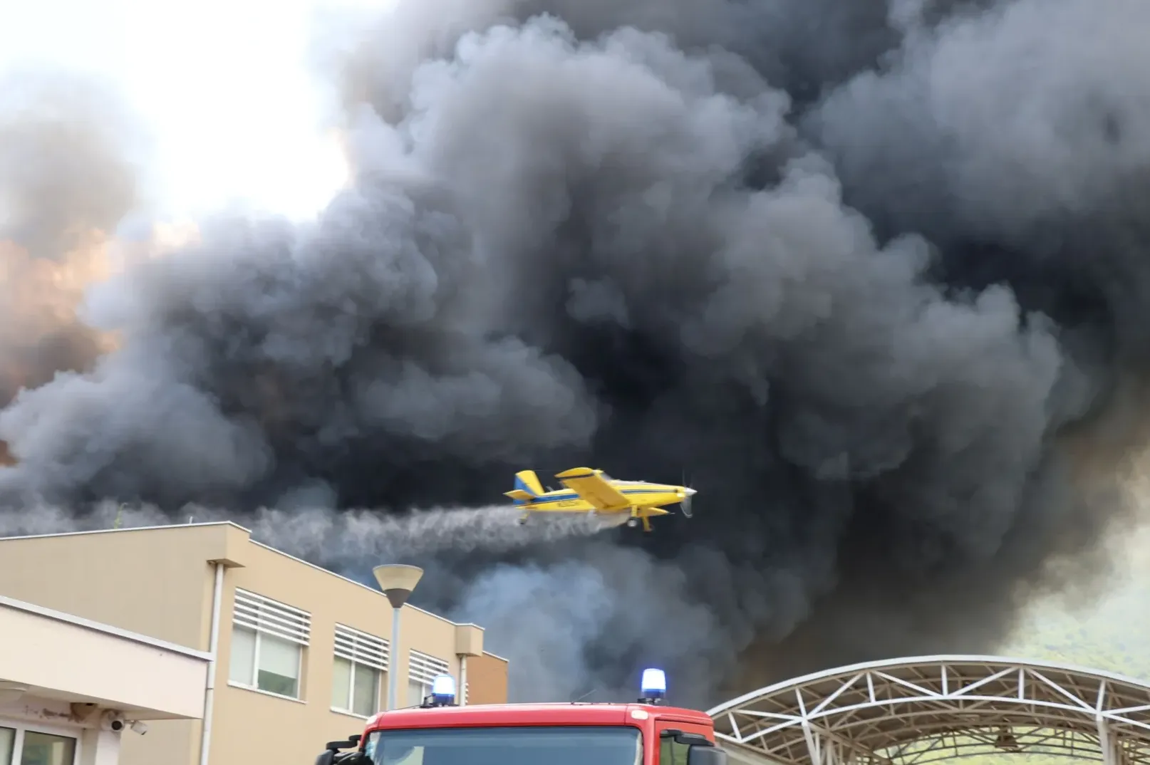 Avion za gašenje požara leti kroz gusti crni dim iznad zgrade.