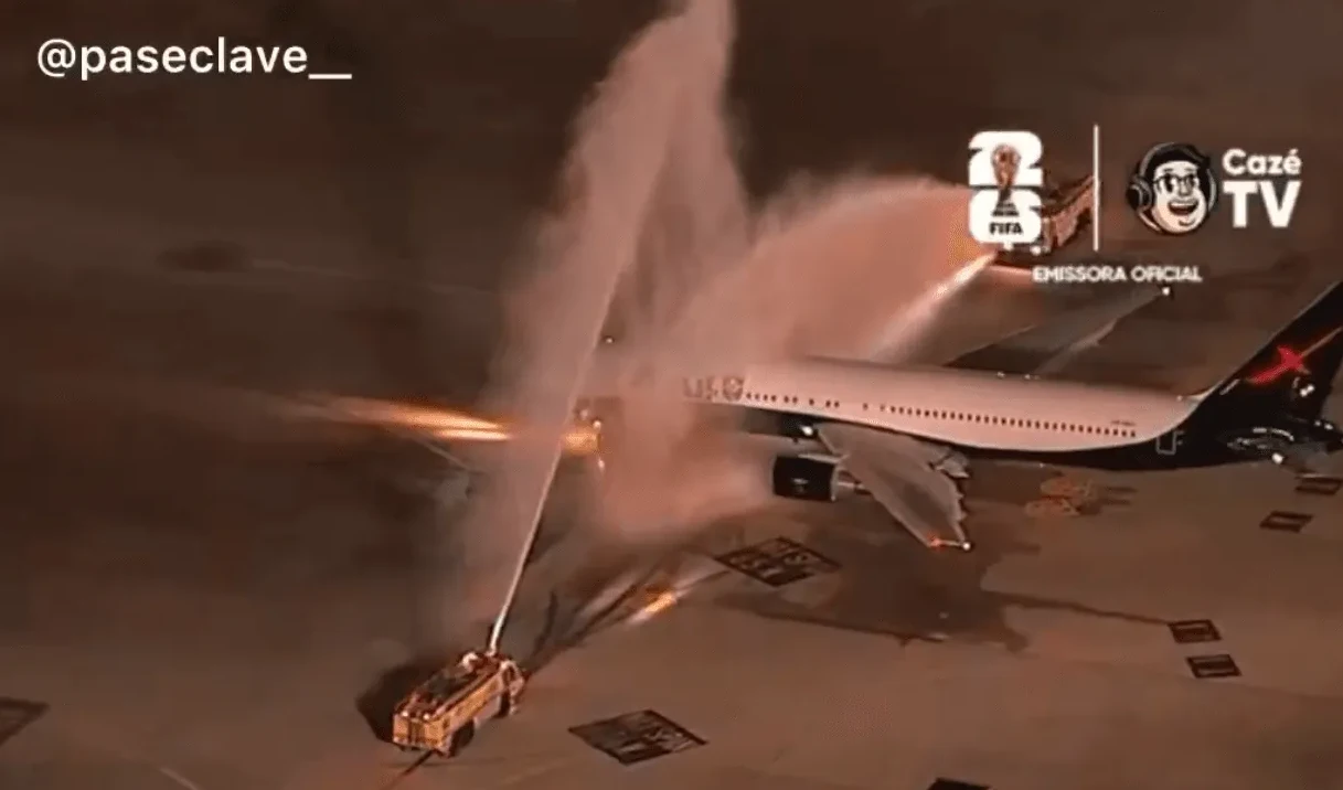 Avion koji prima vodeni pozdrav od vatrogasnih vozila na aerodromu, uz logotip FIFA Svjetskog prvenstva i Caze TV.