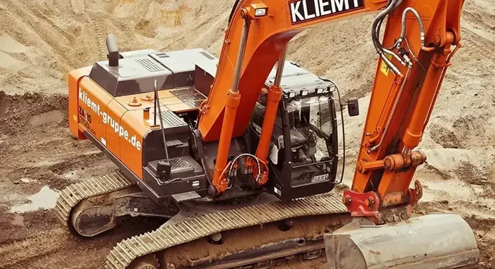 Krupni kadar narandžastog bagera na gradilištu, sa gusjenicama koje se nalaze na zemlji