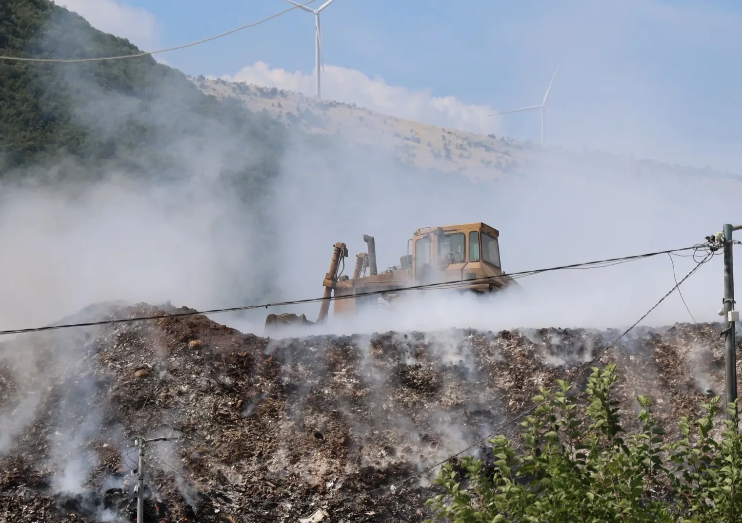 Bager na deponiji smeća koja gori uz prisustvo dima.