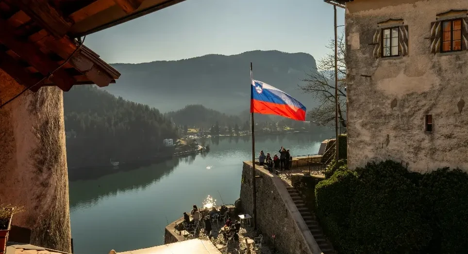 Slovenska zastava na vjetru ispred Bledskog jezera i planina.