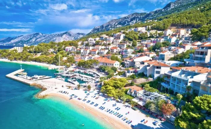 Pogled na obalu sa plažom, marinom sa jahtama i mediteranskim gradom na padini planine