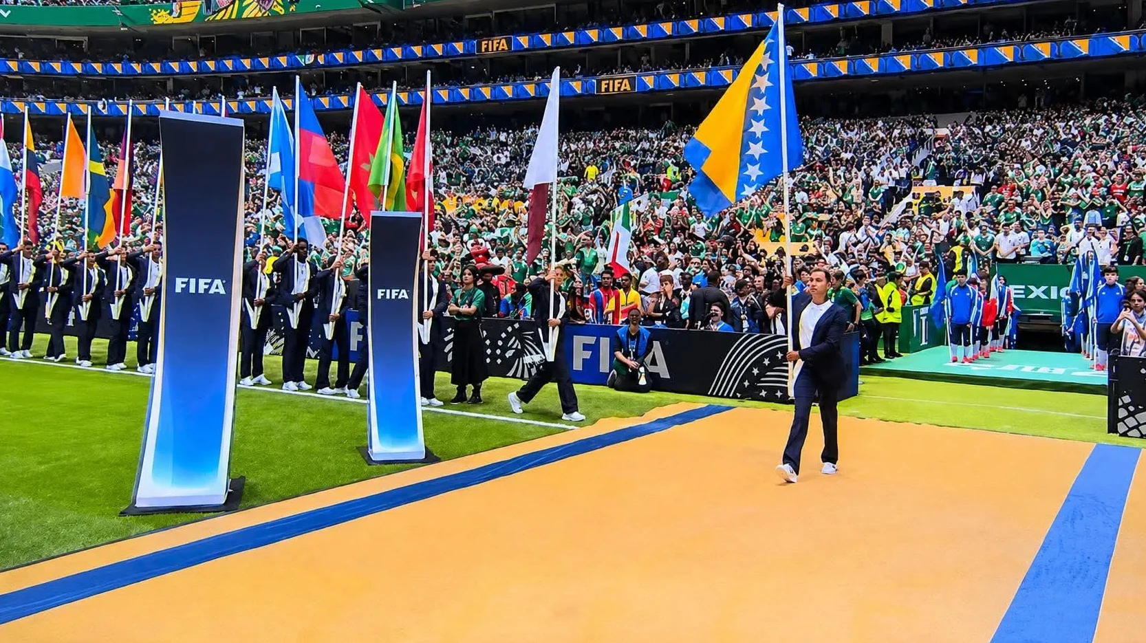 Nosioci zastava zemalja učesnica Svjetskog prvenstva u fudbalu, uključujući zastavu Bosne i Hercegovine, defiluju terenom stadiona pred punim tribinama.