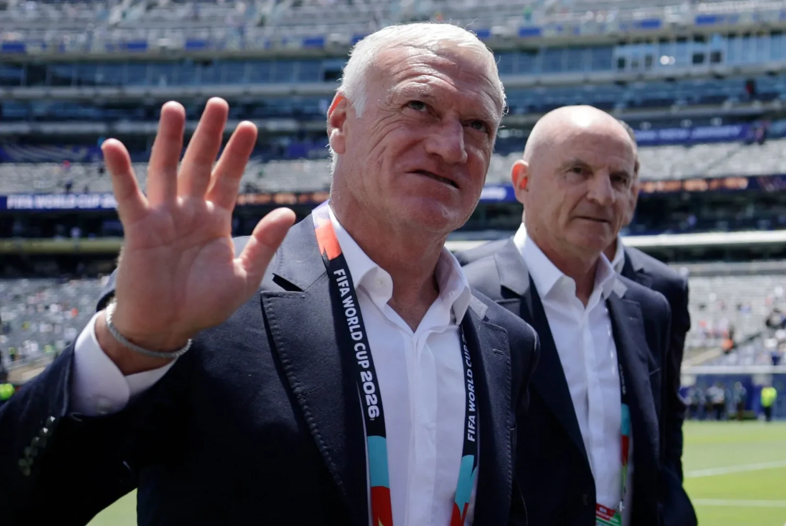 Didier Deschamps maše rukom i nosi FIFA Svjetski kup 2026. oznaku oko vrata.