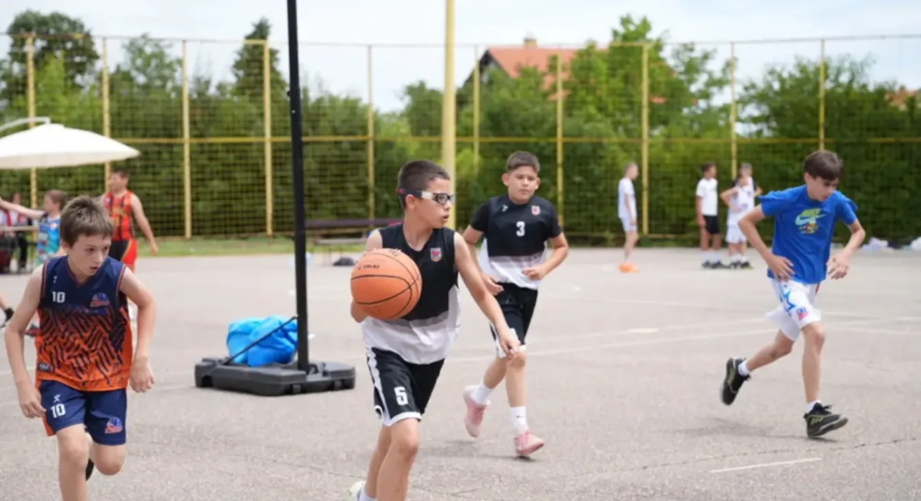 Dječaci u sportskim dresovima trče po košarkaškom terenu dok igraju utakmicu.
