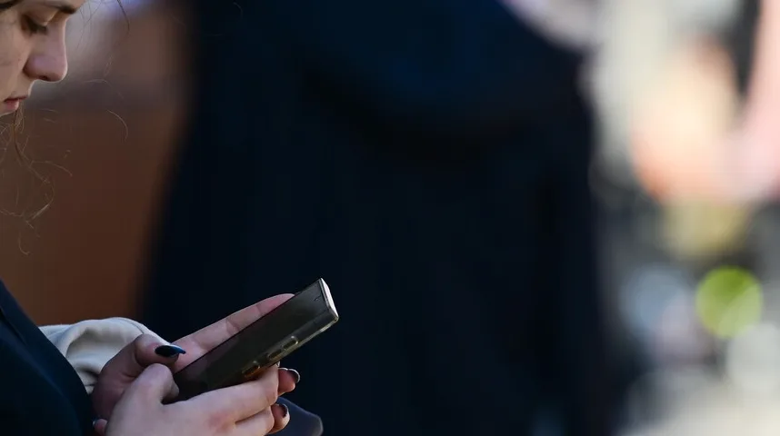 Mlada djevojka drži i gleda u svoj pametni telefon.