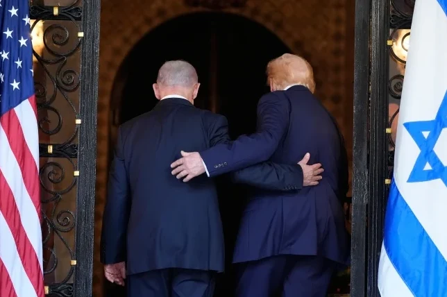 Donald Tramp i Benjamin Netanjahu zagledani u daljinu, Trampova ruka oko Netanjahuovog ramena, zastave SAD-a i Izraela sa strane.
