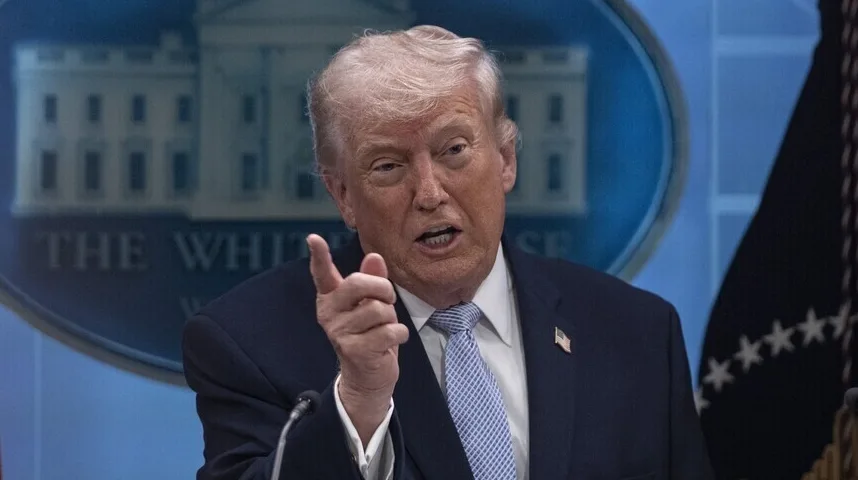 Donald Trump u tamnom odijelu i plavoj kravati, sa znakom Bijele kuće iza njega, govori publici.
