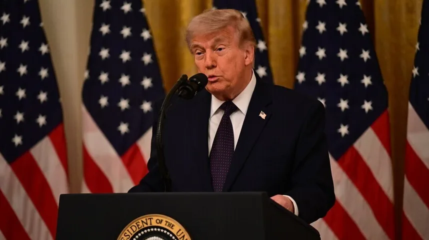 Donald Trump govori za govornicu sa predsjedničkim pečatom SAD-a, a iza njega su zastave Sjedinjenih Američkih Država.