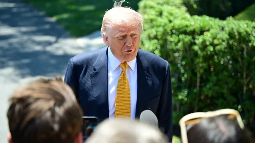 Donald Trump u tamnom odijelu i žutoj kravati govori novinarima vani.
