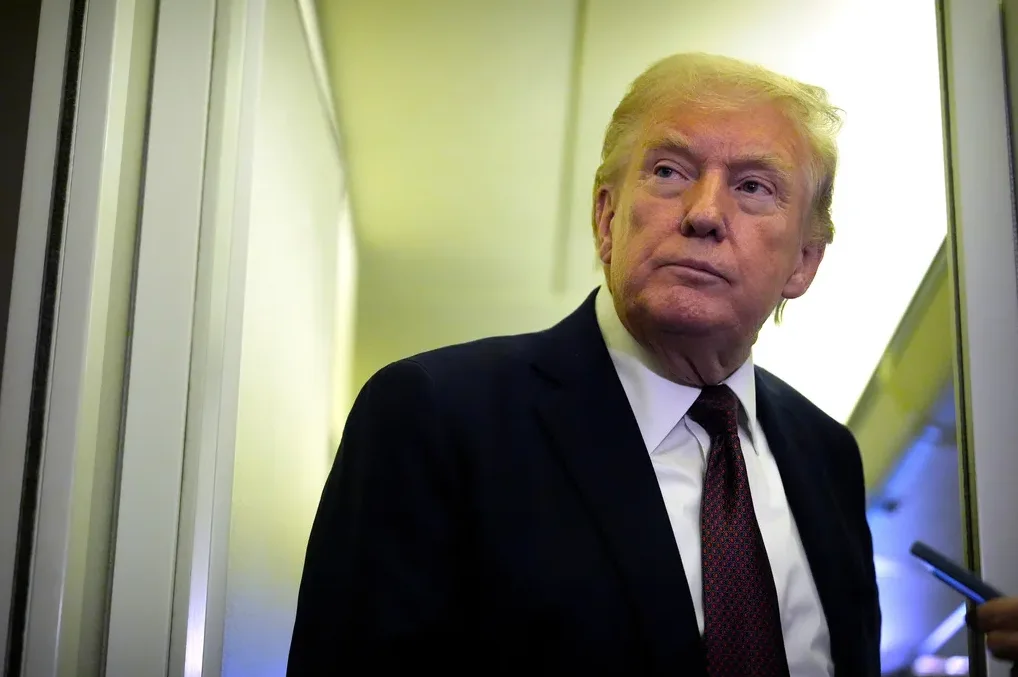 Donald Trump u tamnom odijelu i crvenoj kravati, gleda u stranu unutar aviona.