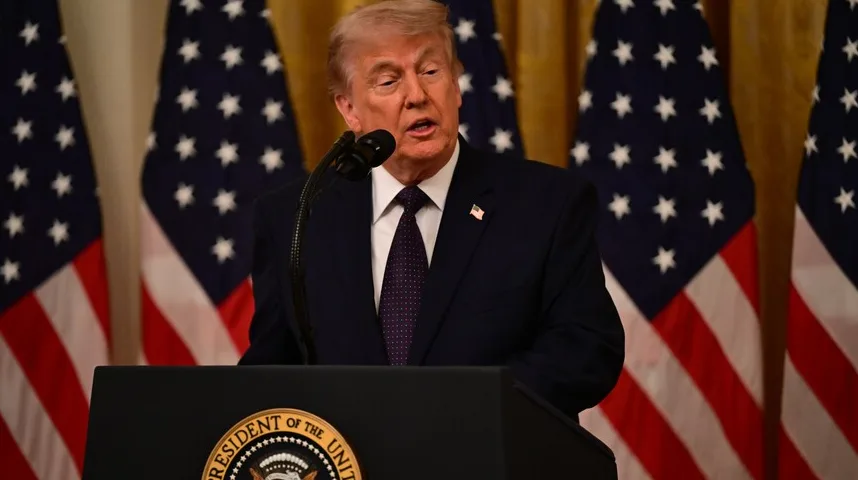 Donald Trump drži govor iza podijuma sa logom Predsjednika Sjedinjenih Američkih Država, dok se iza njega nalaze američke zastave.