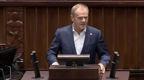 Donald Tusk u tamnoplavom odijelu i bijeloj košulji govori za govornicom u parlamentu.