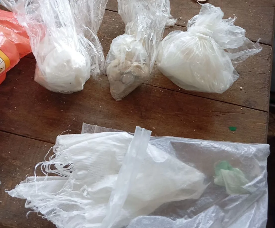 Više plastičnih vrećica s različitim supstancama, poput bijelog praha i grudvica, složenih na drvenom stolu.