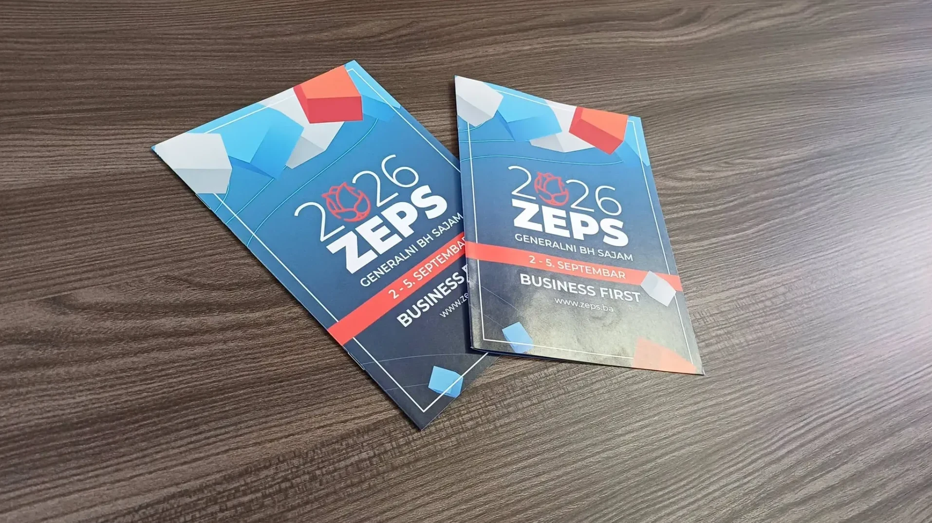 Dva letka za sajam "2026 ZEps Generalni BH Sajam" sa natpisom "Business First" i datumom "2-5. Septembar", postavljena na drvenoj površini.