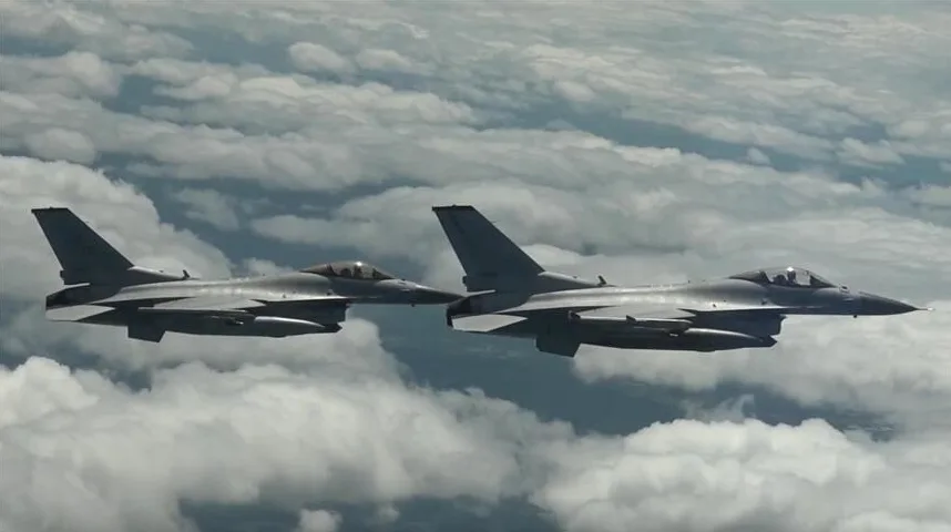 Dva borbena aviona F-16 lete u formaciji visoko iznad gustih oblaka.
