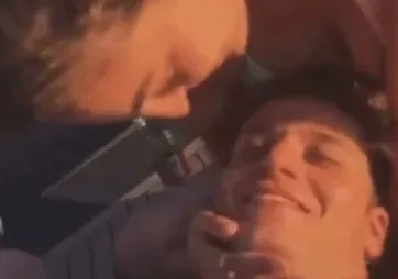 Bliski zagrljaj dvoje mladih osoba, sa fokusom na osmijeh jednog od njih.