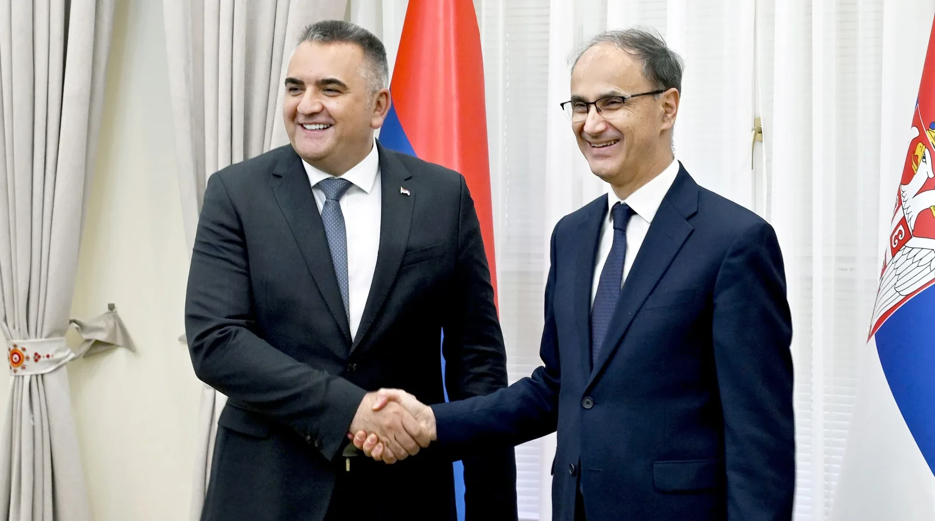 Dva muškarca u odijelima se rukuju ispred zastava Srbije i Republike Srpske.