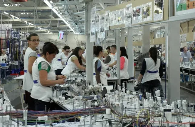 Ženski radnici u bijelim uniformama montiraju električne kablove na proizvodnoj liniji u fabrici.
